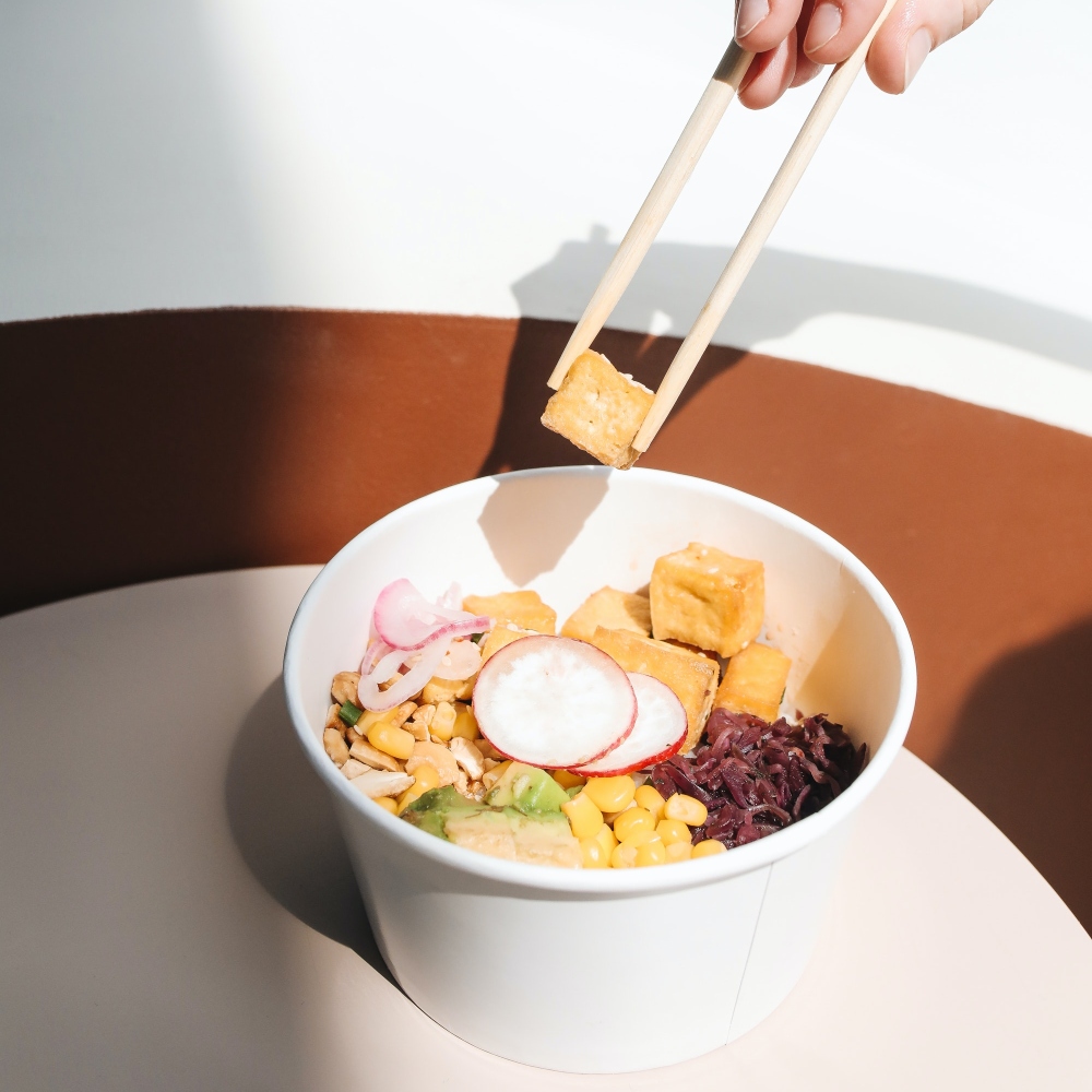 a Person's Hand Getting Tofu from a Poke Bowl