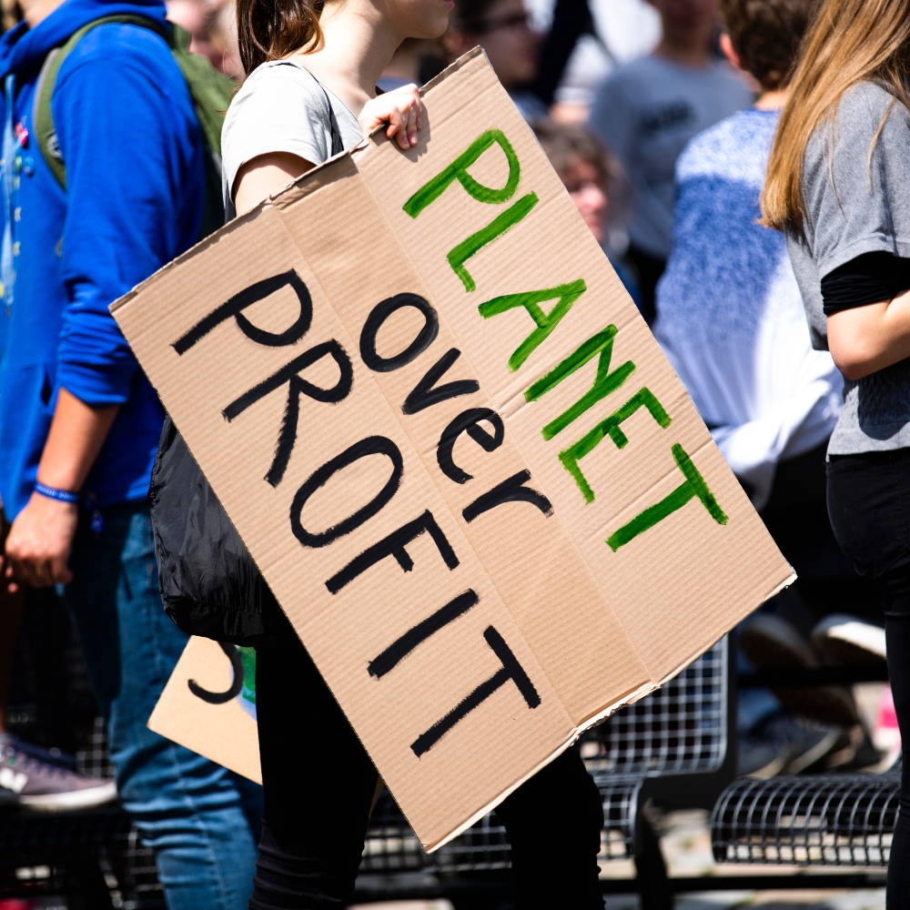 A climate protestor holds a sign that reads planet over profit